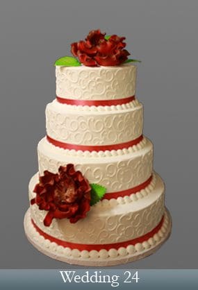 A four layer cake with red ribbon and flowers.