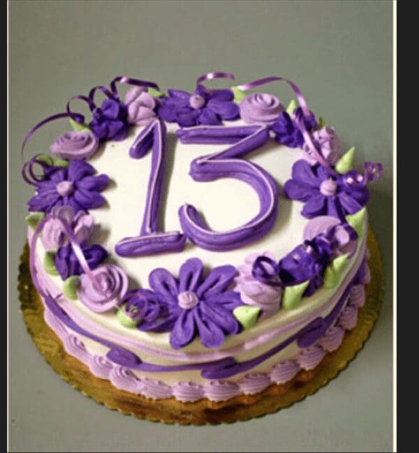 A cake with purple flowers and the number fifteen on it.